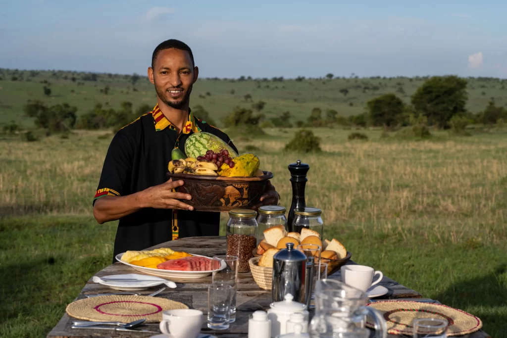 River camp waiter serving fruits for breakfast outdoors - explore bush dining experience