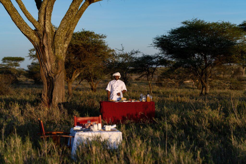 Serengeti camp chef all smiles after setting the table for guests at a bush dining experience